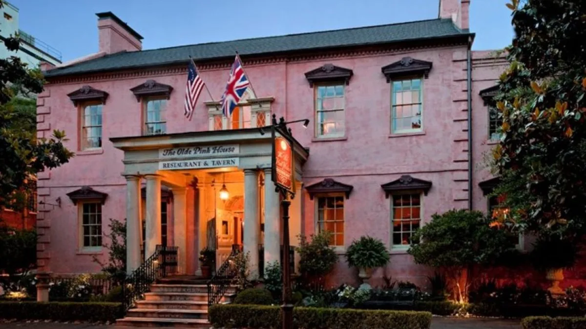 The Olde Pink House Restaurant & Tavern, a pink stucco Georgian mansion glowing at dusk, with American and British flags above its columned entrance.